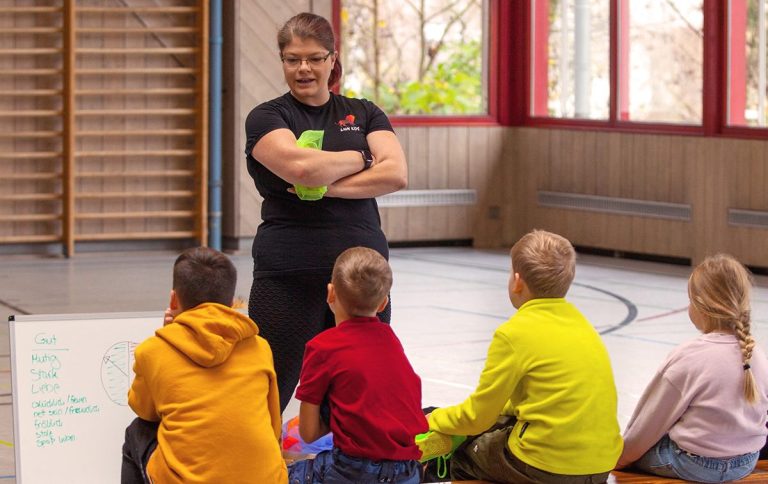 Die Resilienztrainerin Helen Häge spricht zu einer Gruppe von Kindern in einem Sportraum.