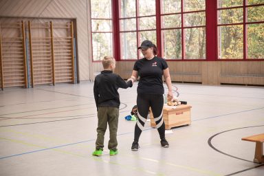 Helen Häge zeigt zusammen mit einem Jungen eine Resilienzübung in einer Sporthalle